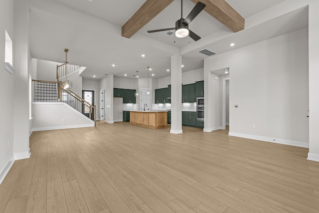 unfurnished living room with light hardwood / wood-style floors, ceiling fan with notable chandelier, and beam ceiling