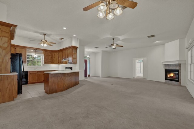 kitchen featuring stove, light carpet, black fridge, a fireplace, and kitchen peninsula