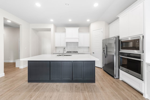 kitchen featuring an island with sink, light wood-type flooring, white cabinetry, appliances with stainless steel finishes, and sink