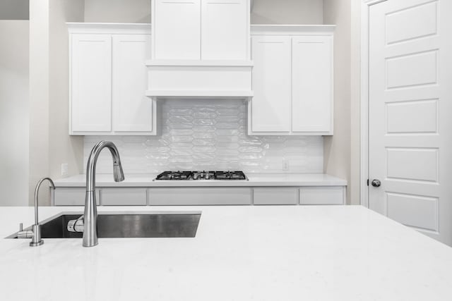 kitchen featuring sink, white gas cooktop, decorative backsplash, and white cabinetry