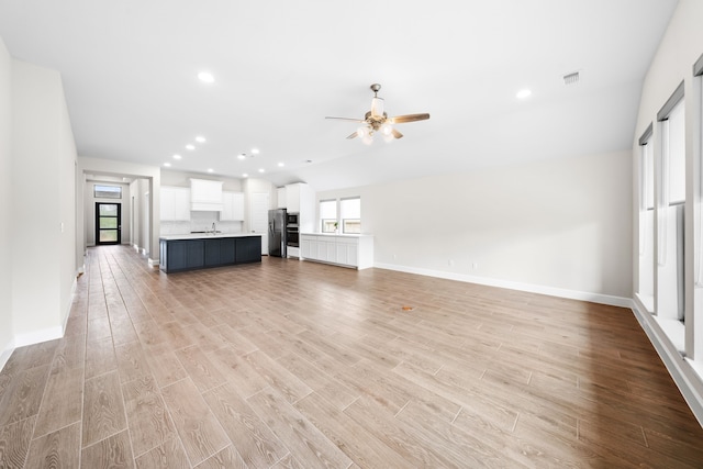 unfurnished living room featuring sink, ceiling fan, vaulted ceiling, and light wood-type flooring