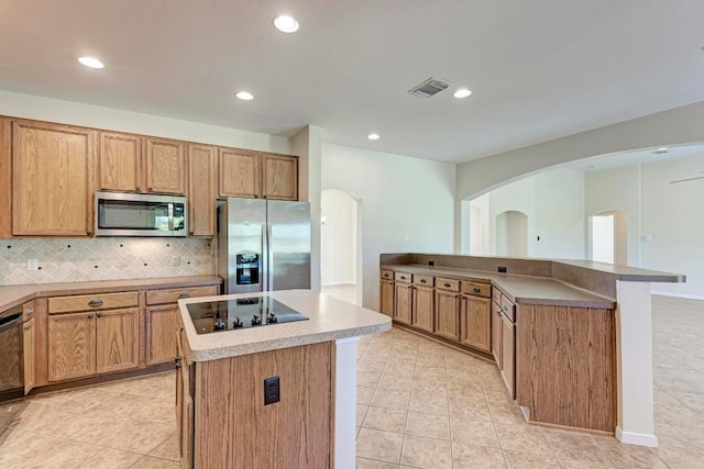 kitchen featuring light tile patterned flooring, decorative backsplash, a kitchen island, and black appliances