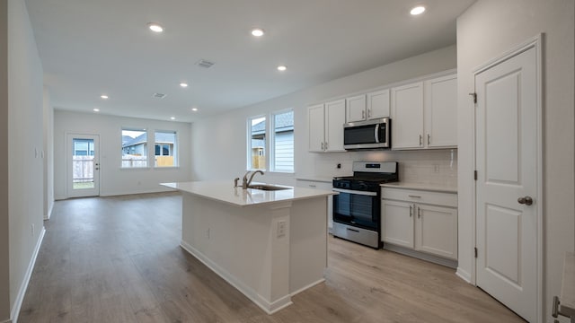 kitchen with an island with sink, sink, white cabinets, and stainless steel appliances