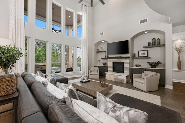 living room featuring dark hardwood / wood-style floors, ceiling fan, a stone fireplace, and a high ceiling