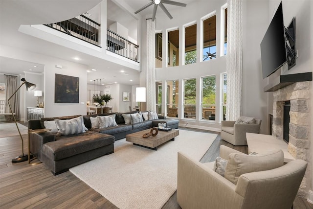 living room featuring a high ceiling, a stone fireplace, ceiling fan, and wood-type flooring