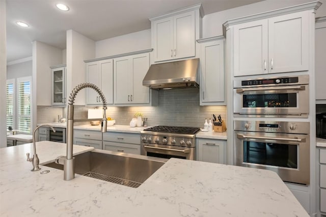 kitchen with decorative backsplash, light stone counters, stainless steel appliances, crown molding, and sink