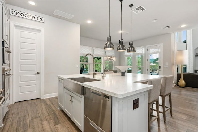 kitchen with pendant lighting, light stone countertops, an island with sink, white cabinetry, and stainless steel appliances