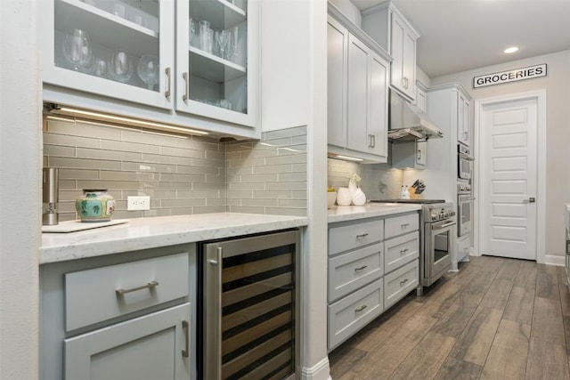 kitchen featuring light stone countertops, stainless steel range, dark wood-type flooring, beverage cooler, and backsplash