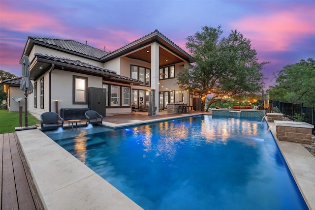 pool at dusk featuring pool water feature, a patio, and a hot tub