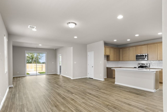 kitchen featuring a center island with sink, sink, appliances with stainless steel finishes, tasteful backsplash, and light hardwood / wood-style flooring