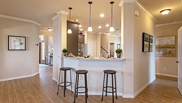 kitchen with hanging light fixtures, crown molding, light stone countertops, stainless steel fridge, and a breakfast bar