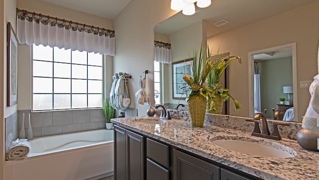 bathroom with vanity with extensive cabinet space, dual sinks, and a bath