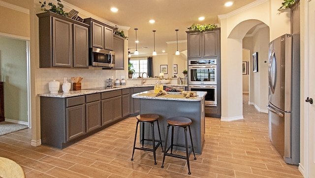 kitchen featuring tasteful backsplash, a center island, ornamental molding, appliances with stainless steel finishes, and pendant lighting