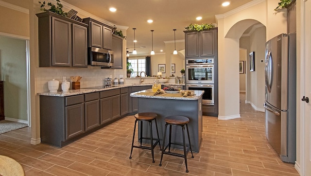 kitchen featuring a center island, hanging light fixtures, ornamental molding, appliances with stainless steel finishes, and backsplash