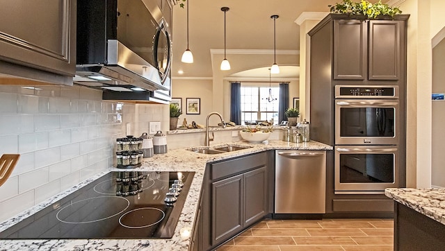 kitchen with hanging light fixtures, ornamental molding, appliances with stainless steel finishes, sink, and tasteful backsplash