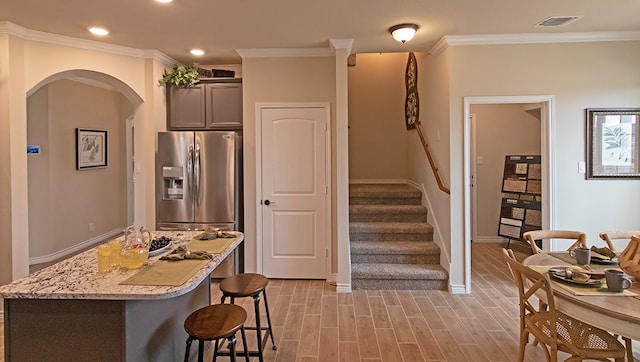 kitchen featuring stainless steel fridge with ice dispenser, ornamental molding, gray cabinetry, and a kitchen bar