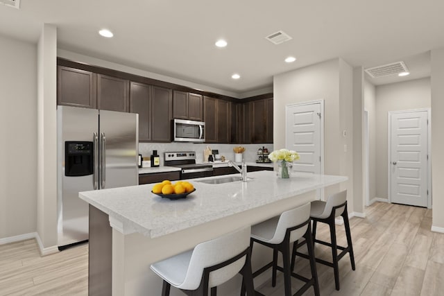 kitchen with appliances with stainless steel finishes, sink, a center island with sink, light hardwood / wood-style flooring, and a breakfast bar area