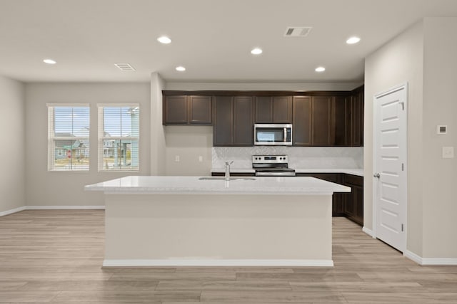 kitchen with sink, light stone countertops, an island with sink, light hardwood / wood-style floors, and stainless steel appliances