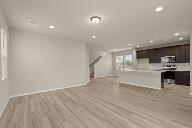 kitchen with decorative backsplash, appliances with stainless steel finishes, dark brown cabinetry, a kitchen island with sink, and light hardwood / wood-style floors