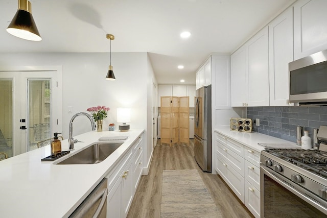 kitchen featuring light wood-type flooring, pendant lighting, white cabinetry, appliances with stainless steel finishes, and sink