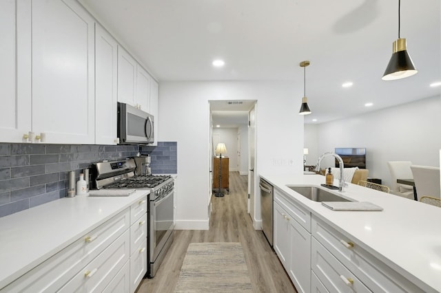 kitchen with stainless steel appliances, decorative light fixtures, light hardwood / wood-style flooring, sink, and white cabinets