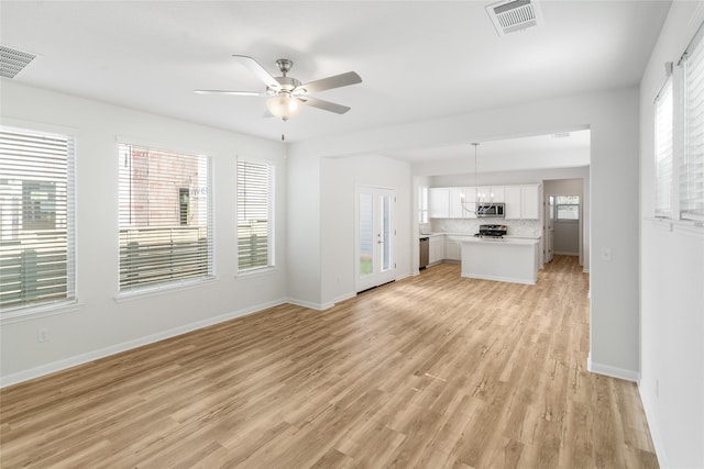 unfurnished living room featuring light wood-type flooring, a healthy amount of sunlight, and ceiling fan with notable chandelier