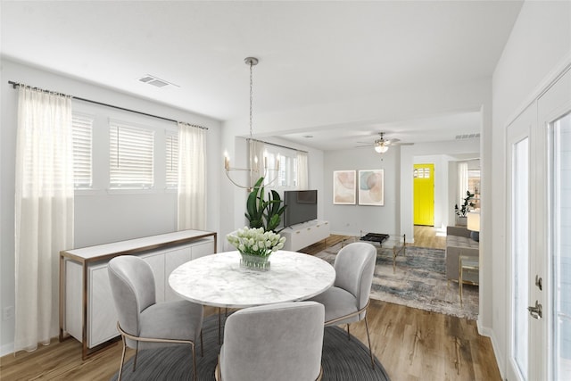 dining space featuring light wood-type flooring and ceiling fan with notable chandelier