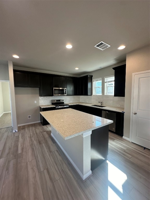 kitchen with light stone countertops, light wood-type flooring, stainless steel appliances, sink, and a kitchen island