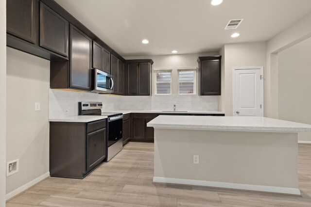 kitchen featuring appliances with stainless steel finishes, sink, decorative backsplash, a center island, and light hardwood / wood-style floors