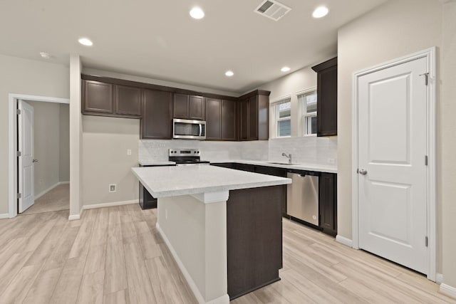 kitchen with sink, light hardwood / wood-style flooring, appliances with stainless steel finishes, a kitchen island, and decorative backsplash