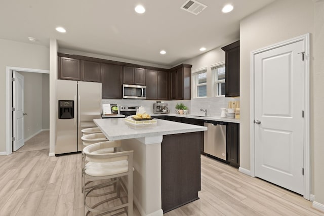 kitchen with stainless steel appliances, dark brown cabinets, a center island, and sink