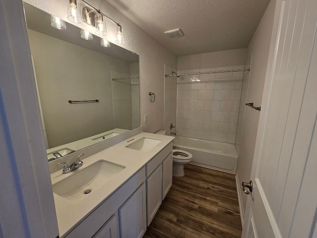 full bathroom with tiled shower / bath, vanity, wood-type flooring, a textured ceiling, and toilet