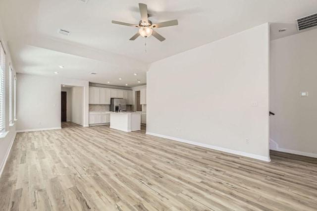 unfurnished living room featuring a ceiling fan, visible vents, light wood finished floors, and baseboards