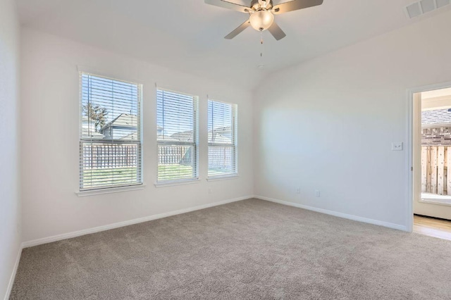 spare room featuring visible vents, baseboards, ceiling fan, vaulted ceiling, and light carpet