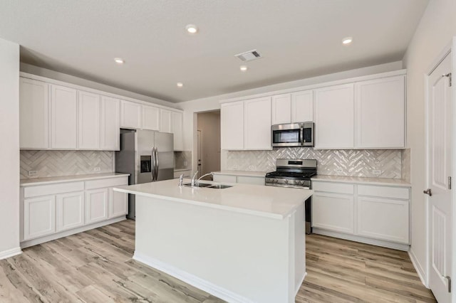 kitchen featuring light wood-type flooring, visible vents, a center island with sink, a sink, and stainless steel appliances