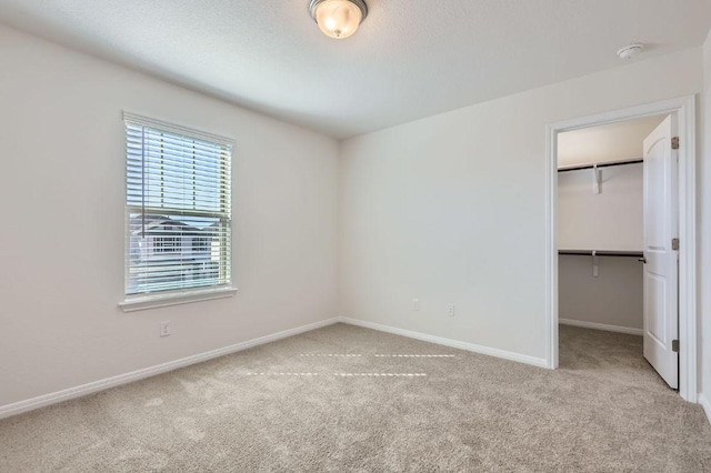 unfurnished bedroom featuring a walk in closet, a closet, baseboards, and carpet floors