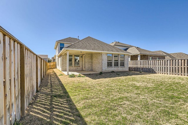 back of property featuring a patio, roof with shingles, a yard, a fenced backyard, and brick siding