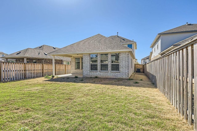 back of property with a yard, brick siding, roof with shingles, and a fenced backyard