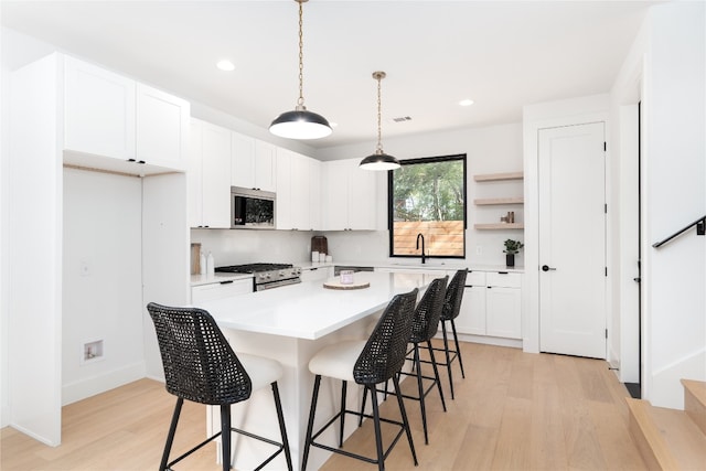 kitchen with appliances with stainless steel finishes, light wood-type flooring, white cabinets, a kitchen island, and hanging light fixtures