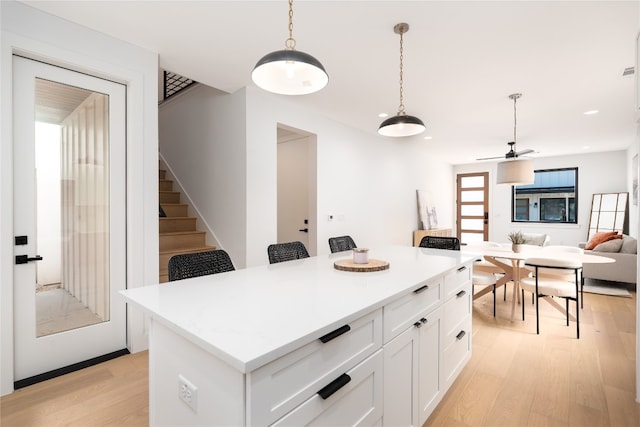 kitchen with hanging light fixtures, a kitchen island, light hardwood / wood-style flooring, a kitchen bar, and white cabinets