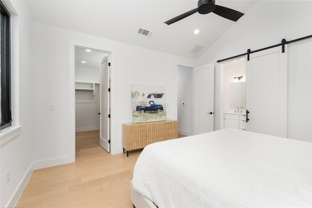 bedroom featuring a walk in closet, ensuite bath, ceiling fan, a barn door, and light hardwood / wood-style floors