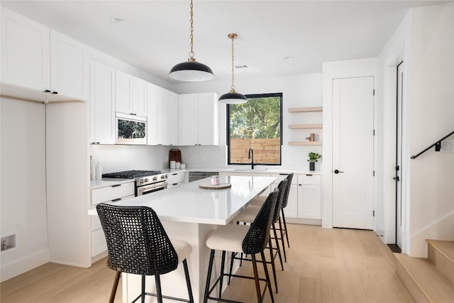 kitchen with stainless steel range with gas cooktop, white cabinetry, and light hardwood / wood-style flooring