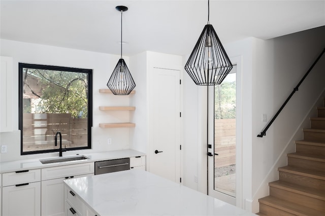 kitchen featuring sink, light stone counters, stainless steel dishwasher, pendant lighting, and white cabinets