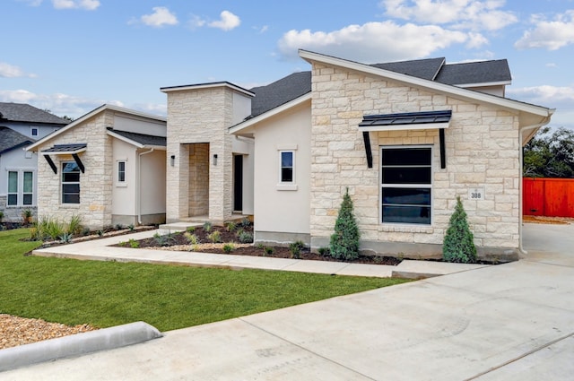 contemporary house featuring a front yard, fence, a shingled roof, and stone siding