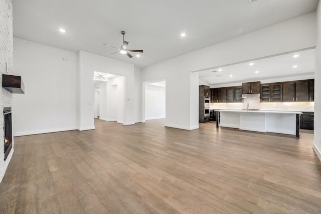 unfurnished living room with wood finished floors, a stone fireplace, baseboards, ceiling fan, and recessed lighting