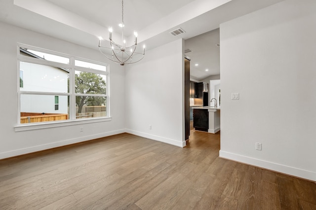 unfurnished room with visible vents, wood finished floors, a sink, baseboards, and a chandelier