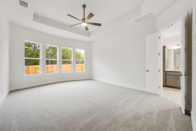 spare room featuring a ceiling fan, light colored carpet, visible vents, and a raised ceiling