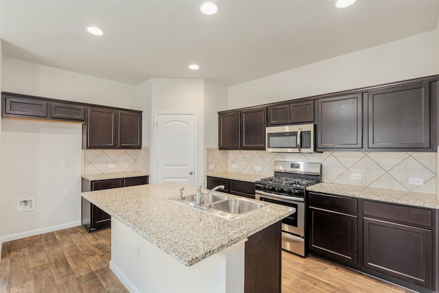 kitchen featuring light stone counters, stainless steel appliances, sink, light hardwood / wood-style flooring, and an island with sink