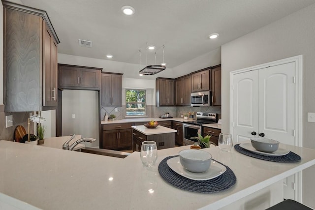 kitchen with visible vents, a center island, a sink, stainless steel appliances, and backsplash