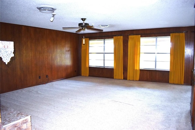 empty room featuring ceiling fan, light colored carpet, a textured ceiling, and wood walls